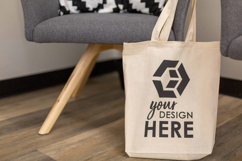 cotton tote bag with logo by a chair